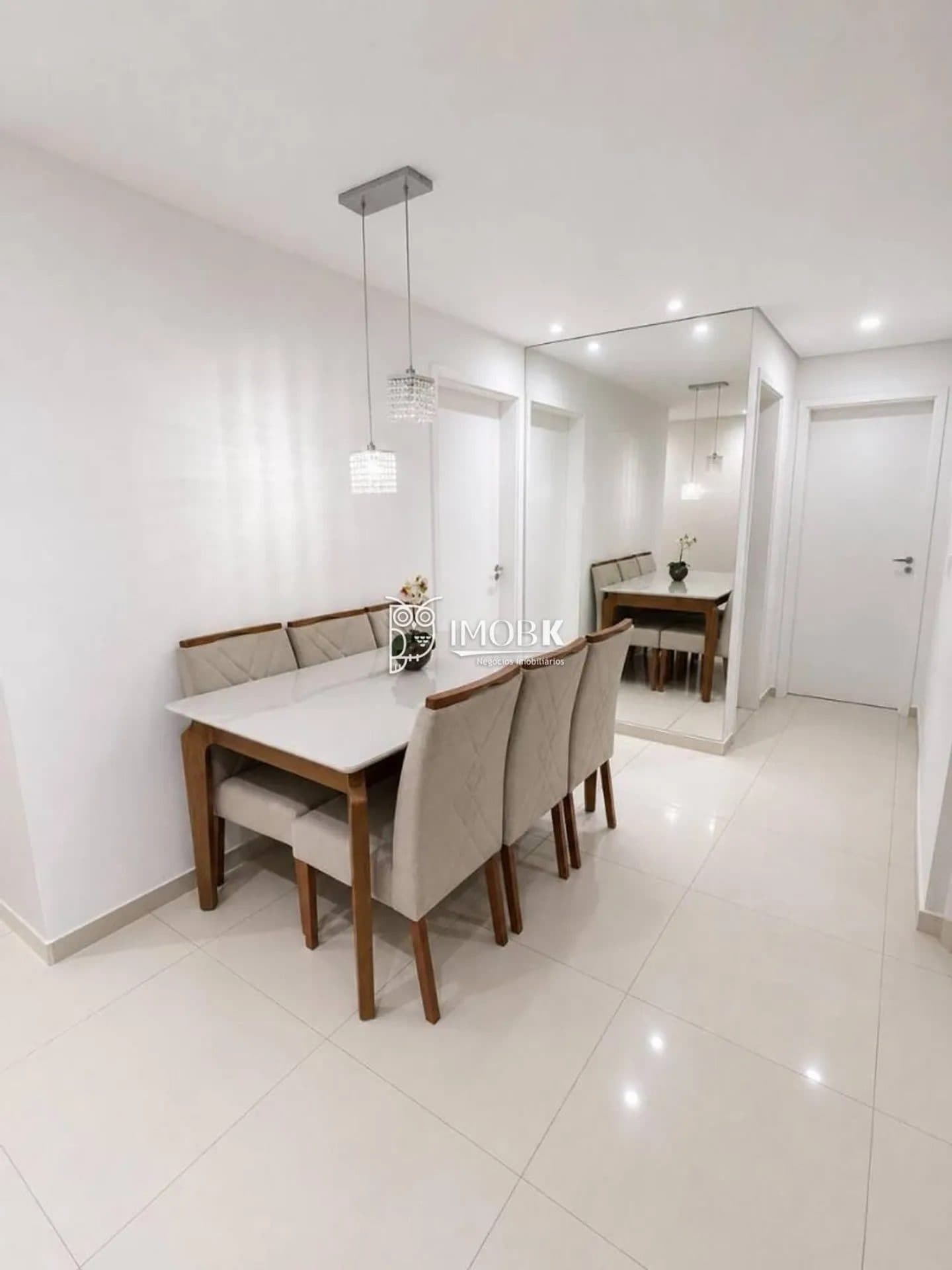 Sala de jantar integrada com mesa de madeira, cadeiras estofadas e parede com espelho.
