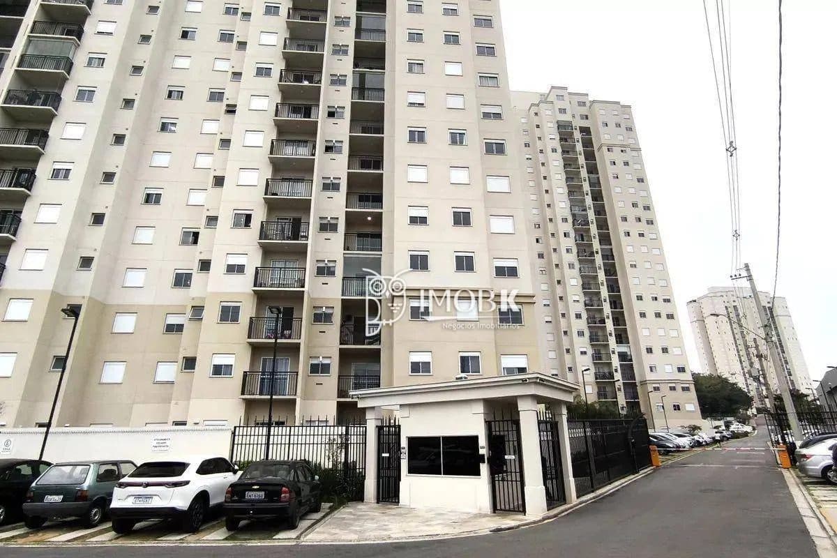 Fachada do condomínio com portaria de acesso, carros estacionados e edifícios altos.