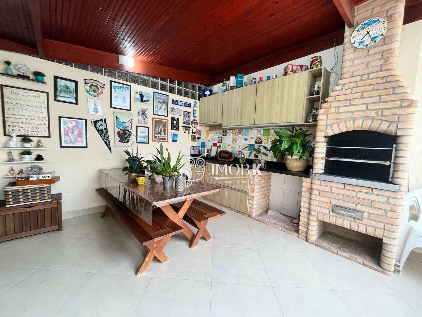 Área gourmet coberta com churrasqueira de tijolos à vista, mesa de madeira e armários.