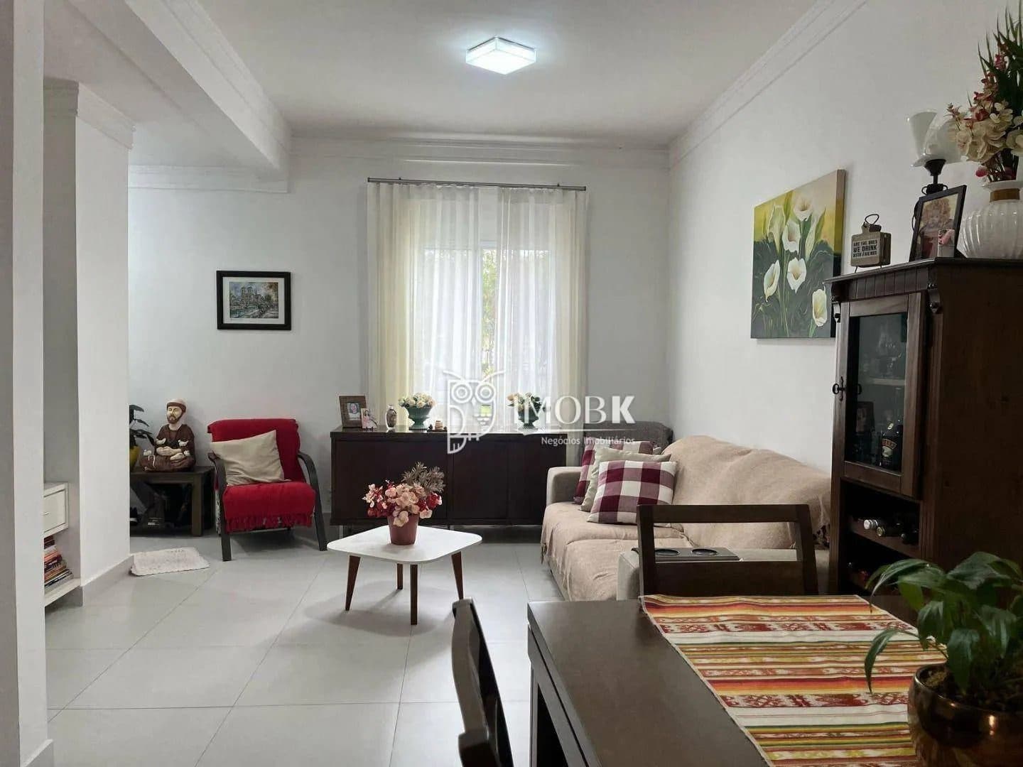 Sala de estar com sofá bege, poltrona vermelha, mesa de centro e piso claro.
