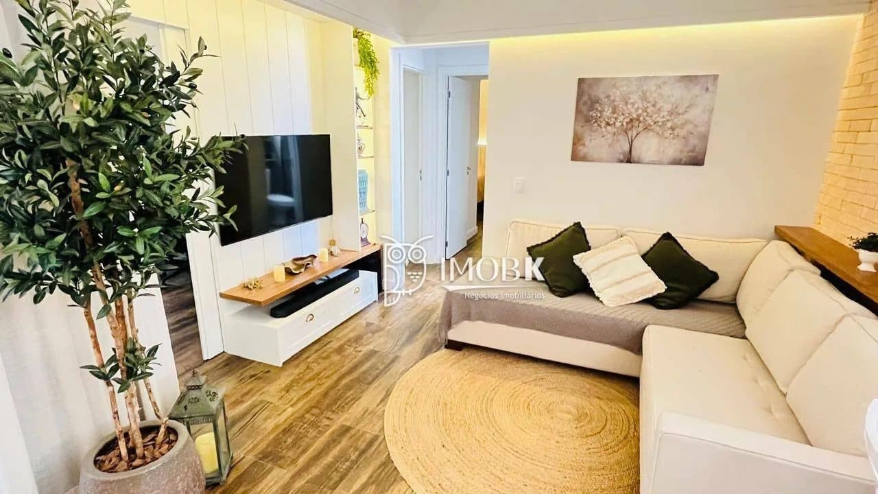 Sala de estar com sofá em L, TV fixada na parede painel amadeirado, tapete redondo e planta decorativa.