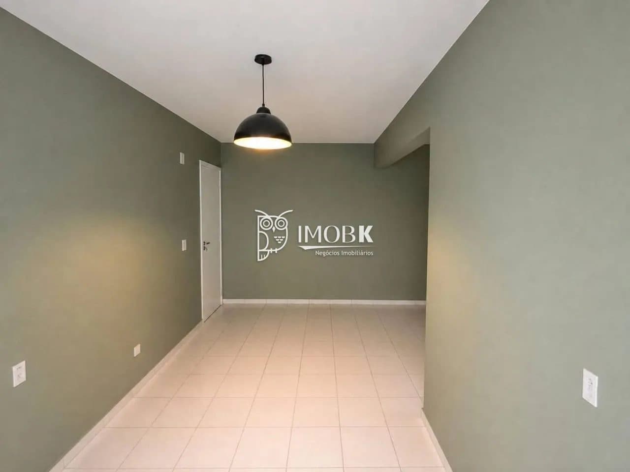 Ambiente de sala vazio com paredes pintadas em tom verde e luminária pendente preta.