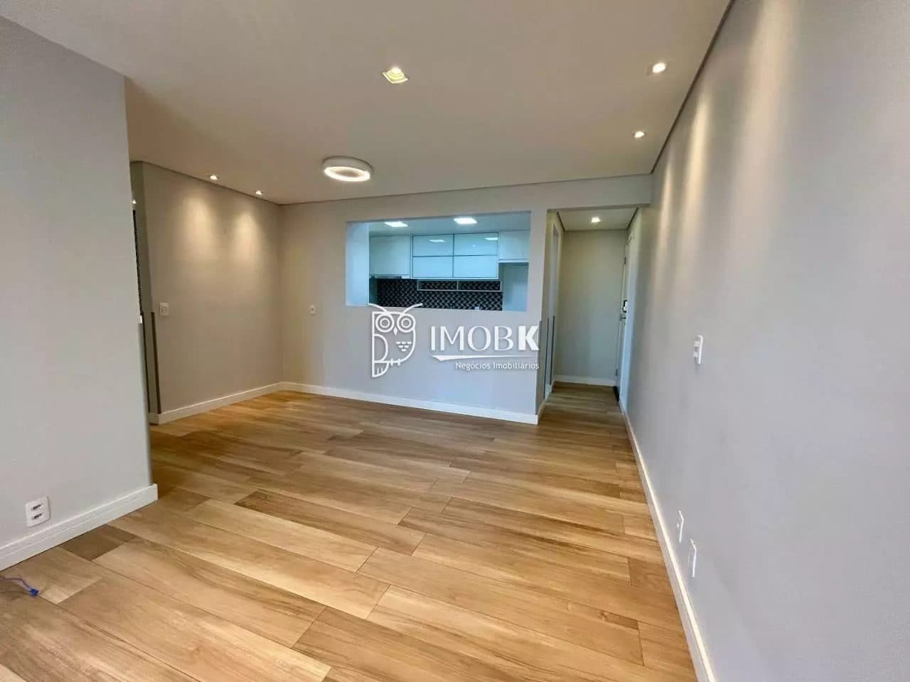 Sala integrada com abertura estilo passa-pratos para a cozinha e piso em tom amadeirado.