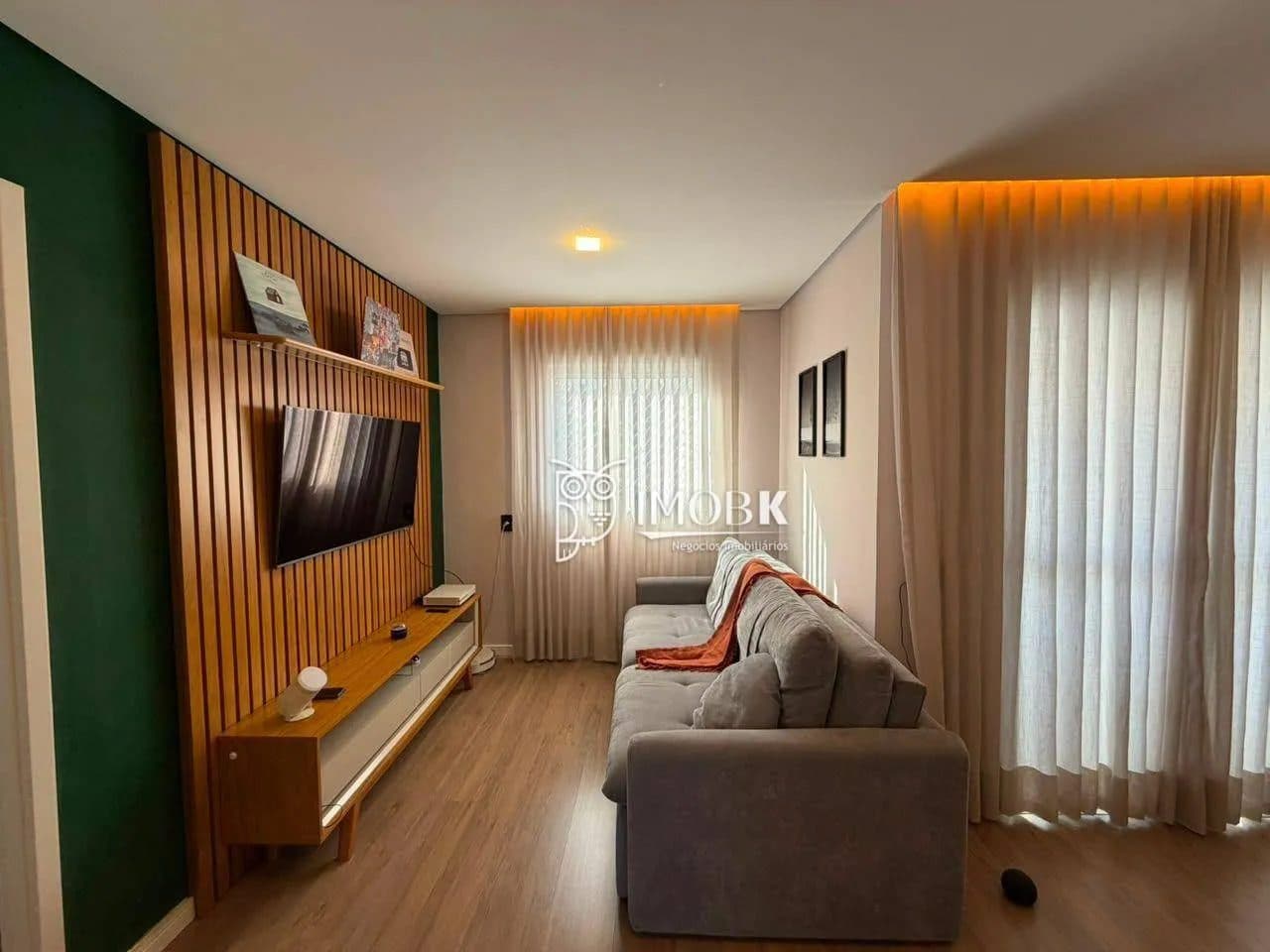 Vista lateral da sala de estar com sofá, painel de TV ripado e cortinas claras