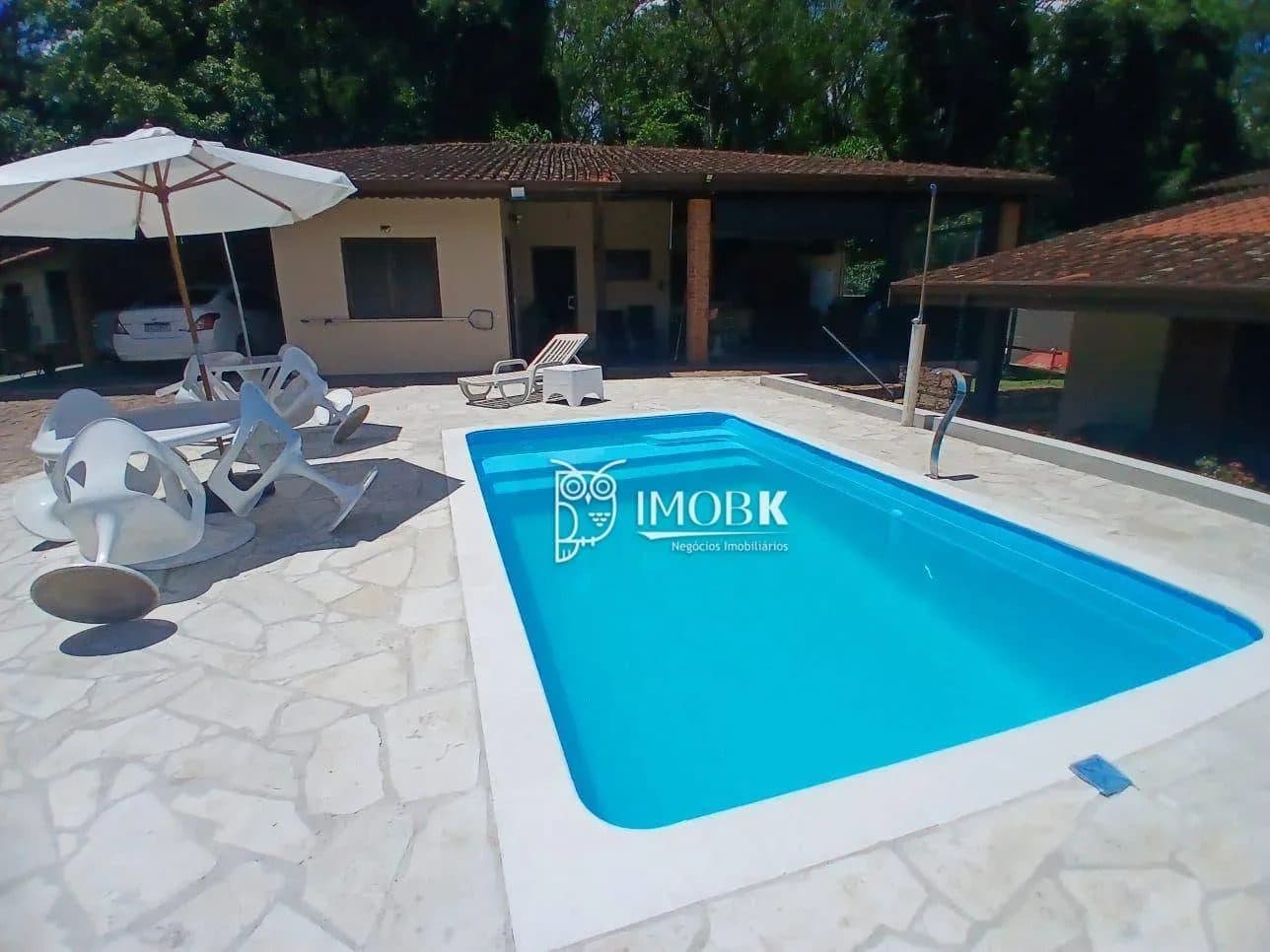 Piscina ao ar livre com piso em pedra e cadeiras de sol