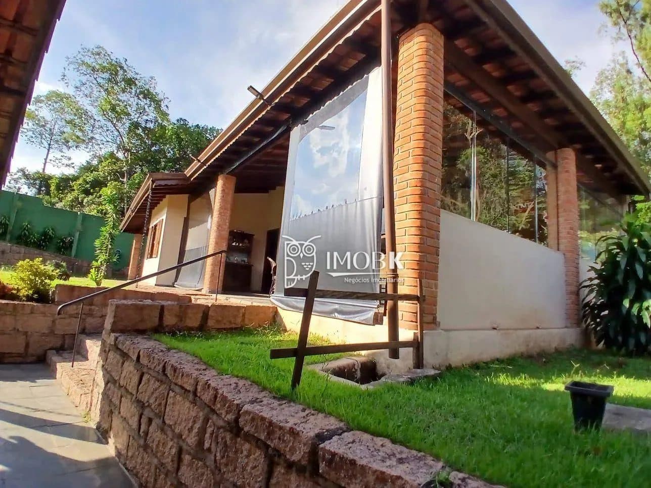 Fachada externa da área de lazer com pilares de tijolos e jardim