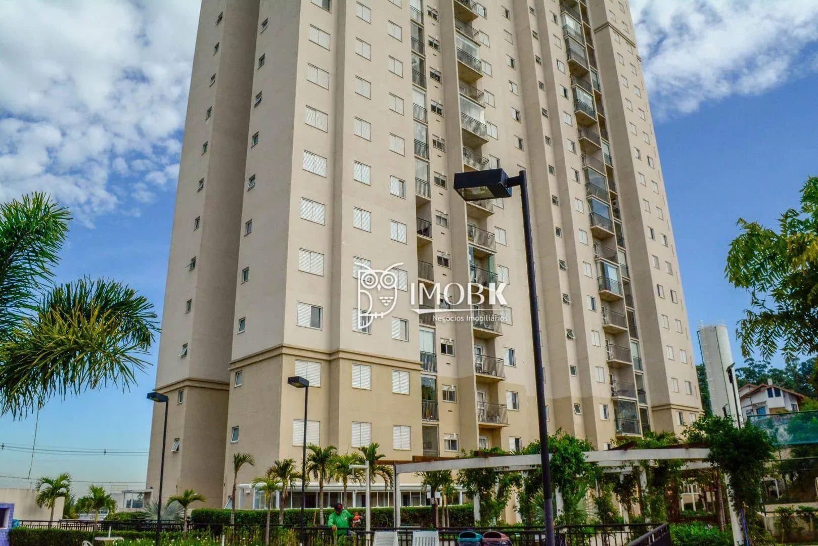 Fachada do edifício residencial com pintura em tons neutros, janelas alinhadas e área verde.