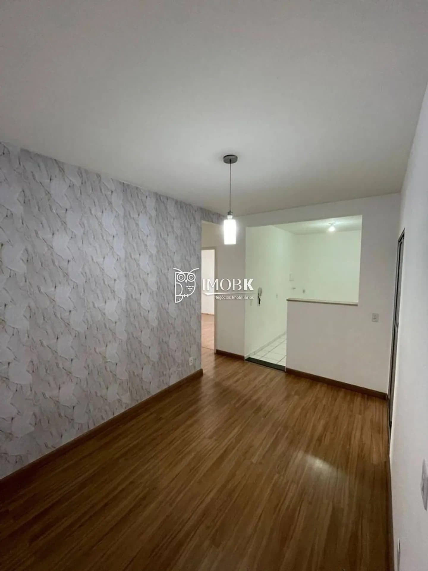 Sala com piso amadeirado, parede com papel de parede texturizado e luminária pendente.