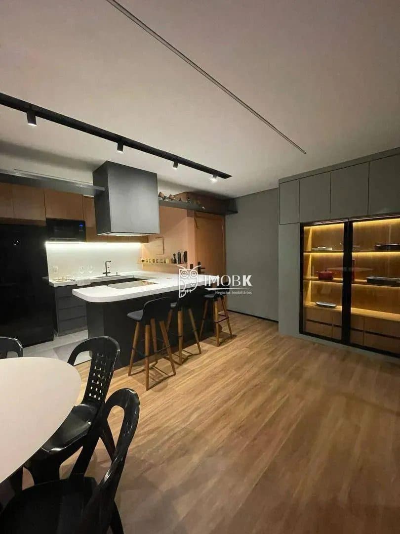 Cozinha com armários planejados escuros, bancada de apoio e iluminação embutida.