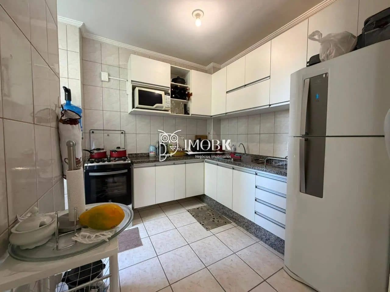 Cozinha compacta com armários brancos, geladeira e bancada em granito.