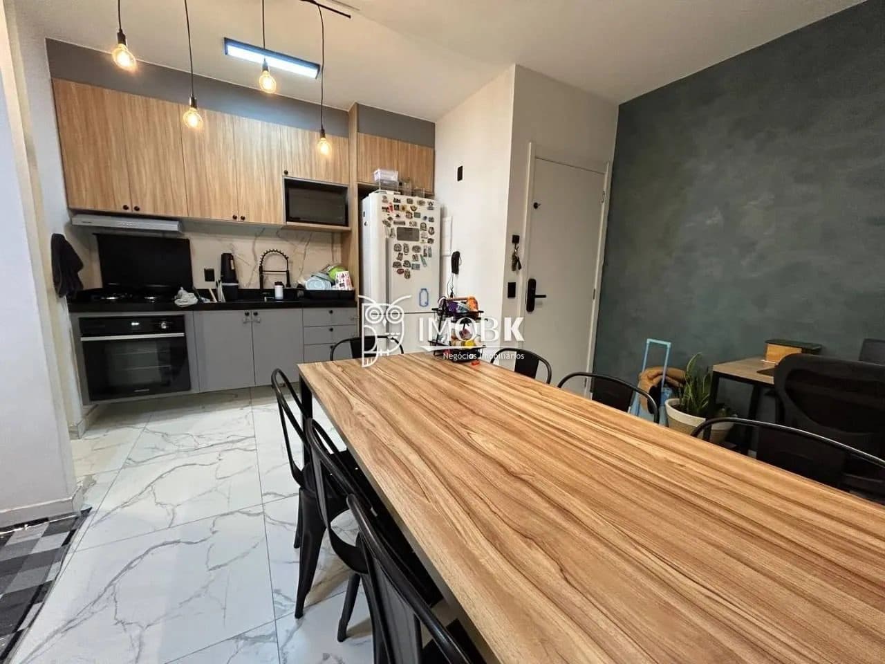Cozinha compacta com armários planejados em tom amadeirado e cinza, bancada escura e mesa de jantar integrada.