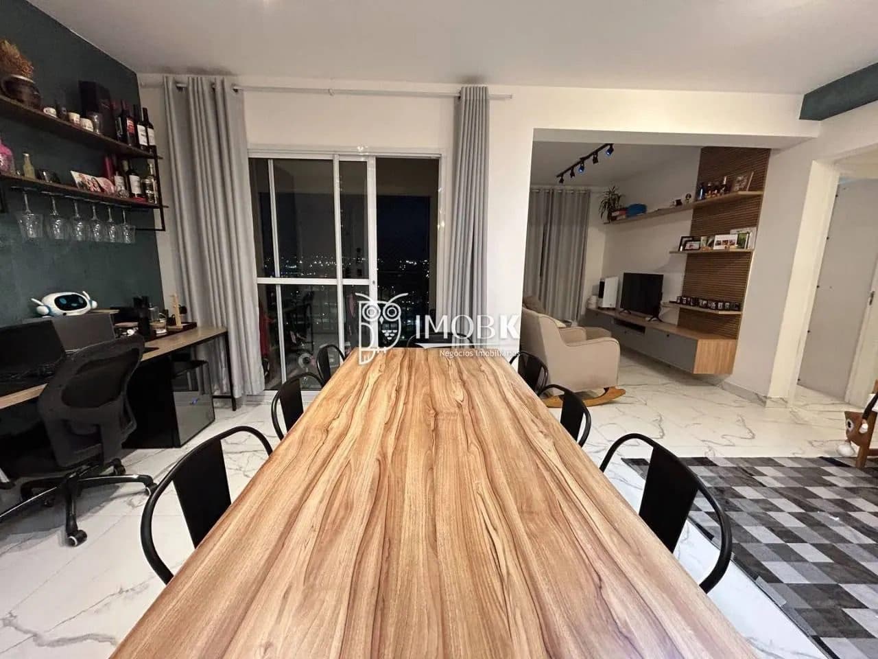 Sala de jantar integrada com espaço de trabalho, mesa grande de madeira e acesso à varanda.