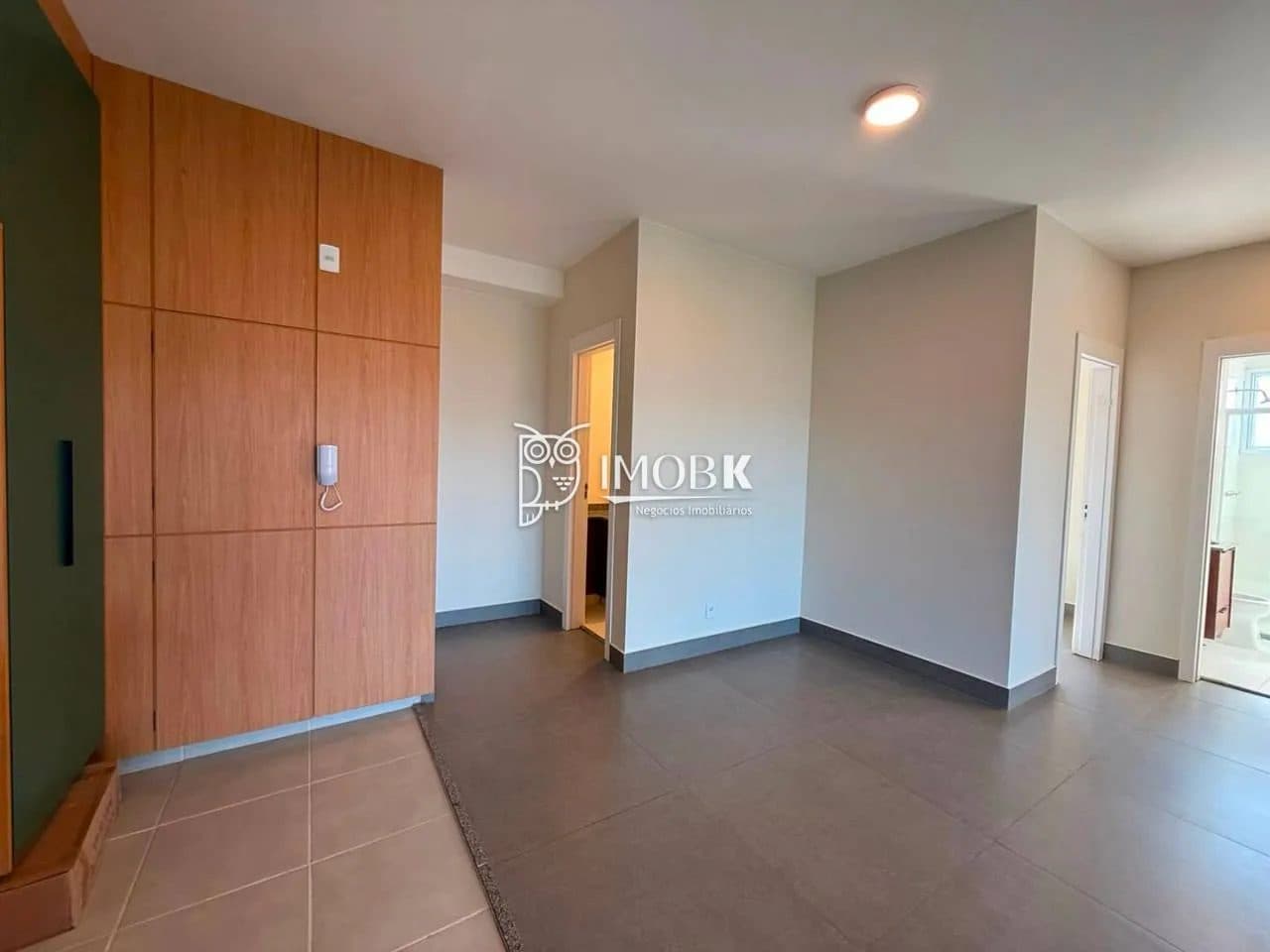 Sala de estar com piso em cerâmica cinza, armário embutido amadeirado e portas internas.