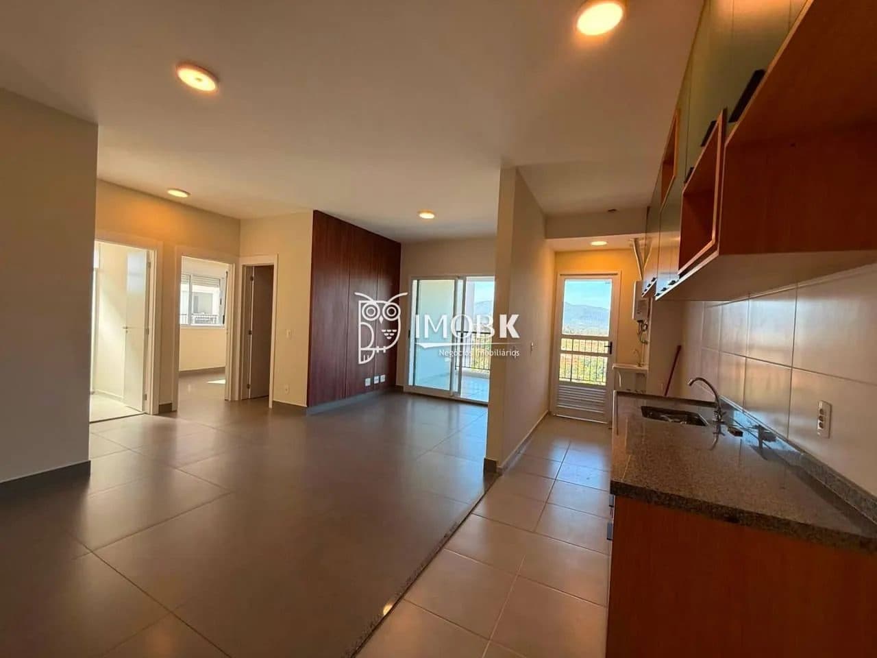 Sala ampla integrada com a cozinha, com acesso à varanda e piso em cerâmica cinza.
