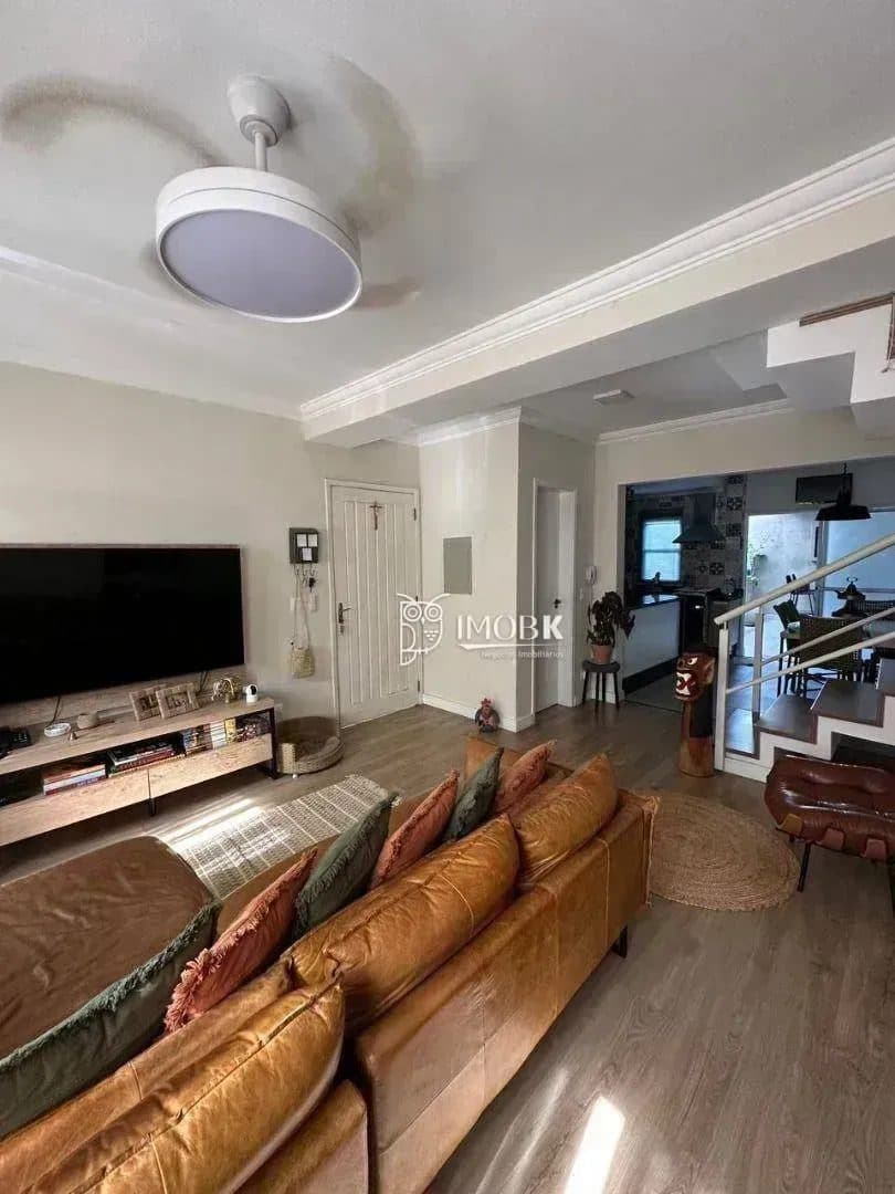 Sala de estar com sofá em couro marrom, rack com TV e piso amadeirado.