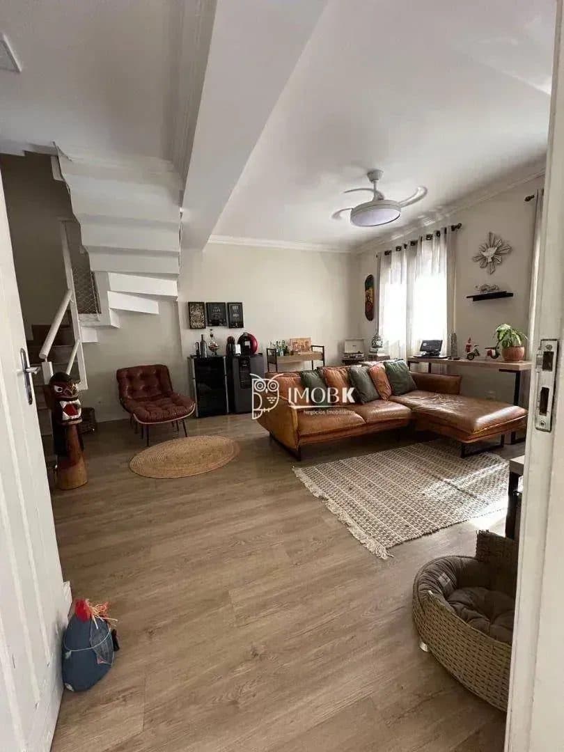Sala de estar com sofá, escada de acesso ao pavimento superior e piso amadeirado.